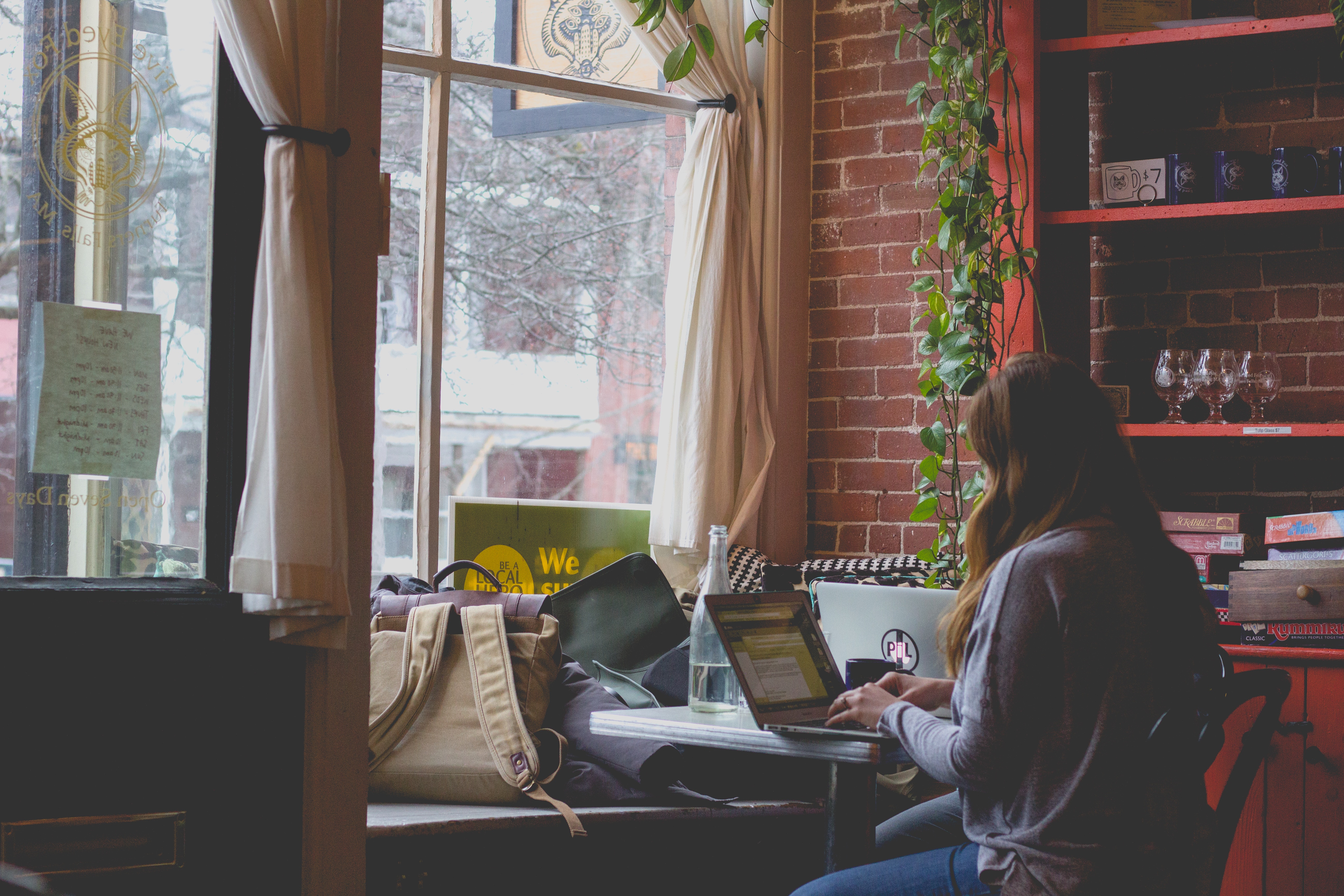 fille dans un café travaillant sur son ordinateur devant une fenêtre, étudiante, travaillante