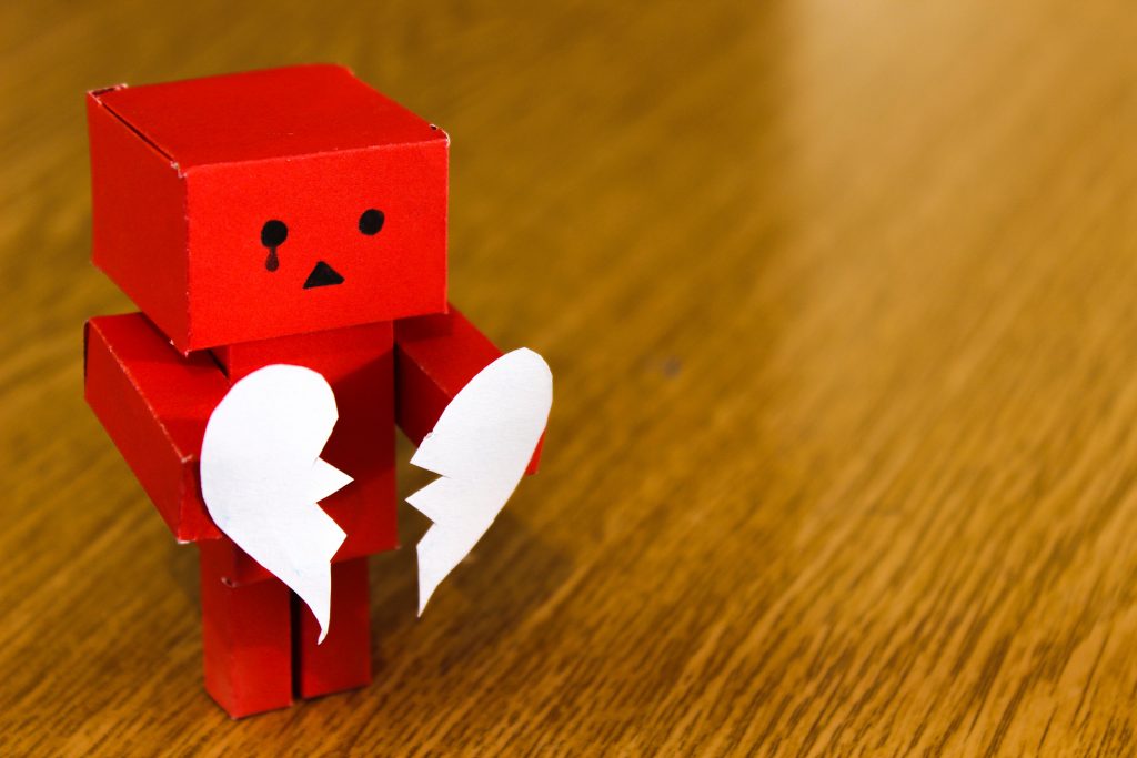 robot rouge avec coeur blanc déchiré en deux, coeur brisé, table de bois