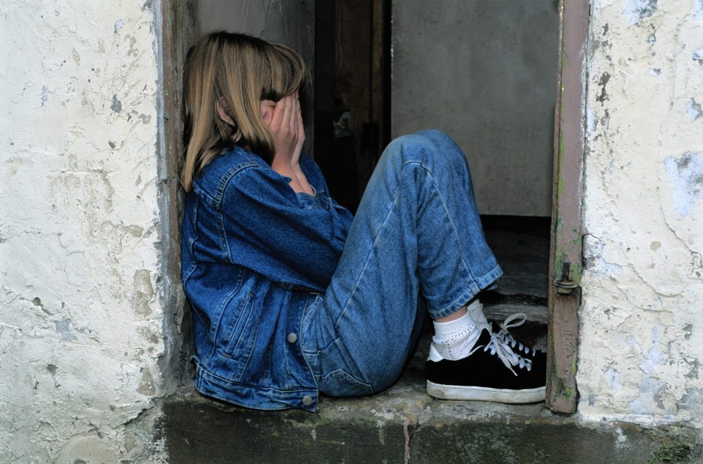 fille qui pleure dans le cadre d'une porte, jeans et veste en jeans