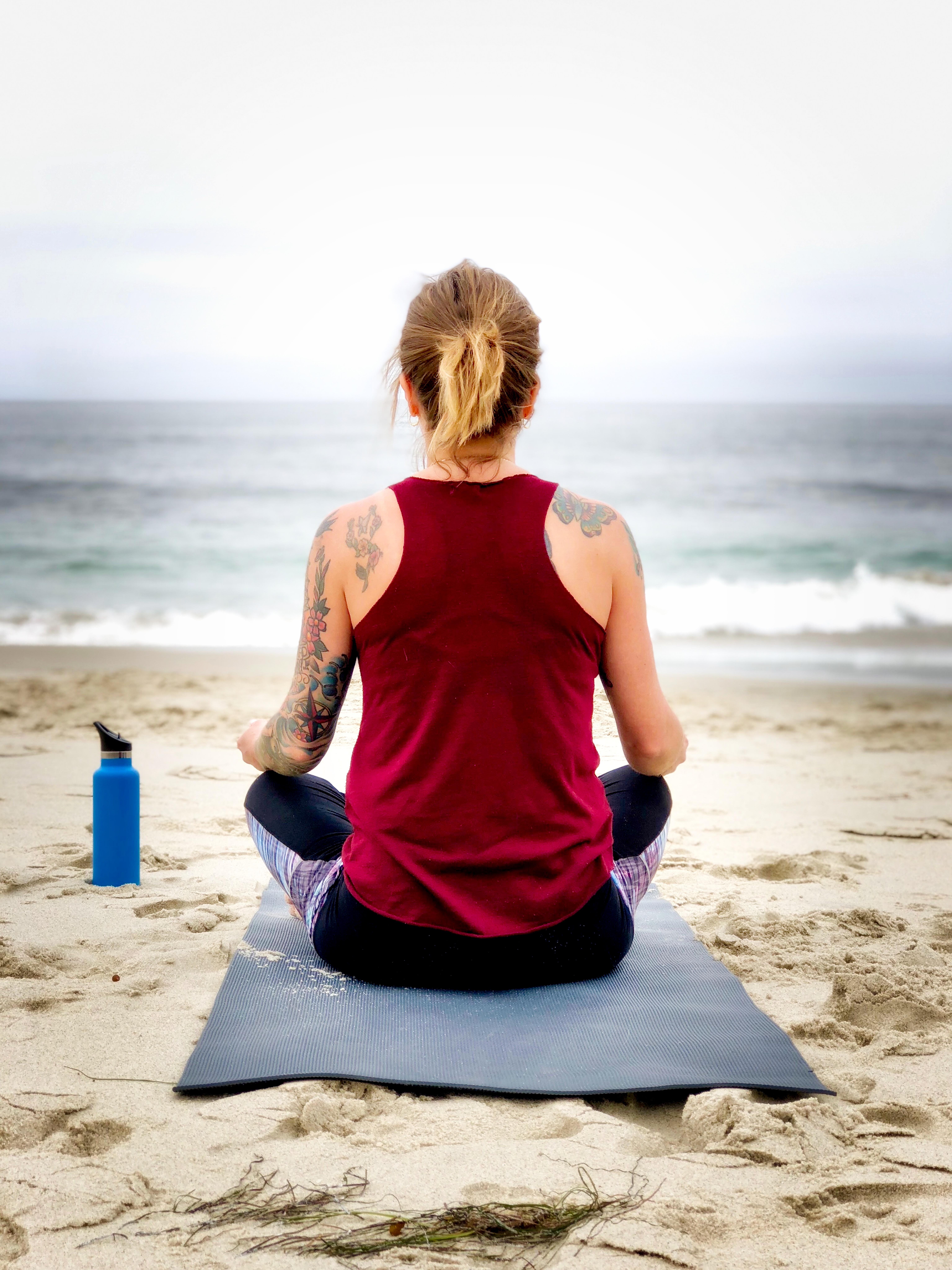 femme faisant du yoga sur la plage de dos sur son matela, bouteille d'eau, océan