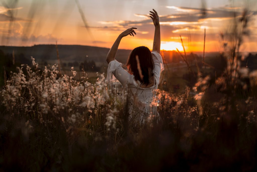 fille qui danse dans un champ de fleurs au coucher du soleil