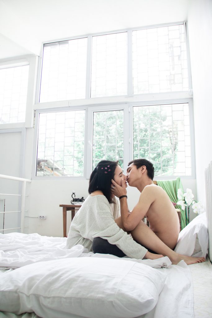 couple qui s'embrasse dans un lit blanc
