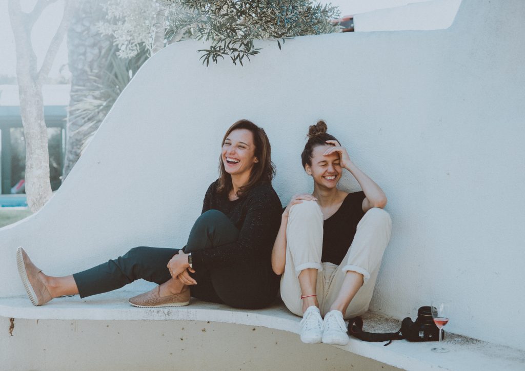 deux femmes qui rient assises contre un mur