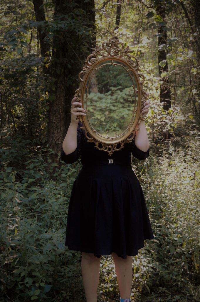 femme robe noire tient miroir forêt