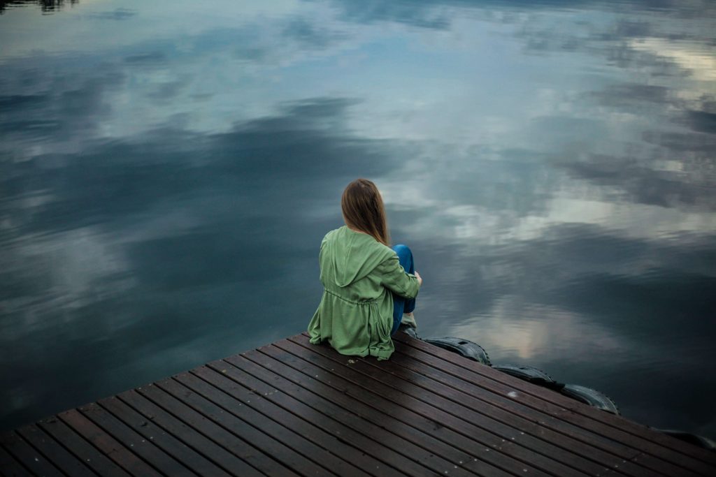 femme assise sur un quai devant un immense lac