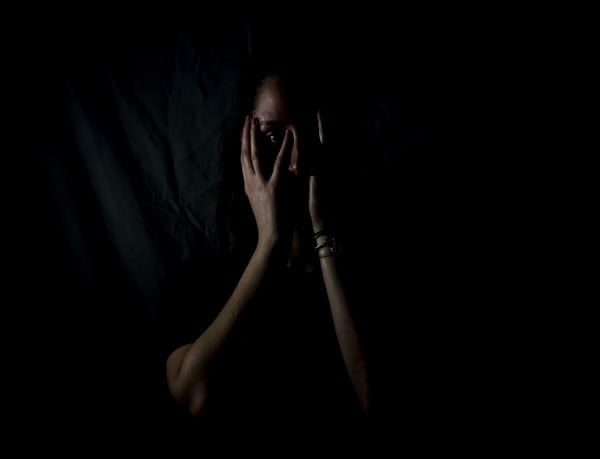 Femme fond noir visage caché par mains peurs