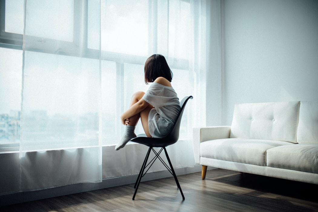 Femme assise sur une chaise noire devant une fenêtre en verre avec des rideaux blancs (nous sommes)